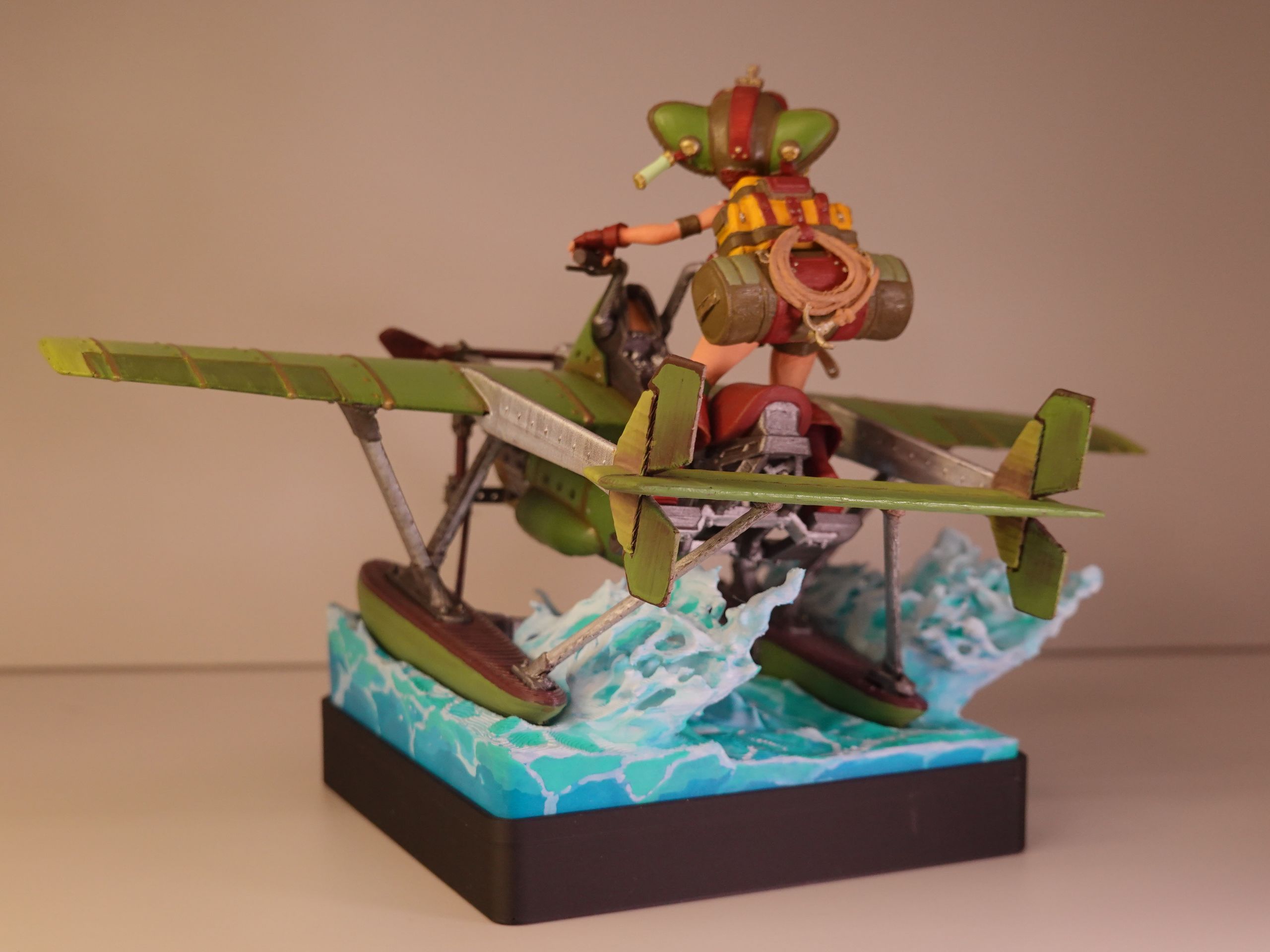 Miniature figure of a character in a green helmet riding a green biplane over a blue base with water effect.
