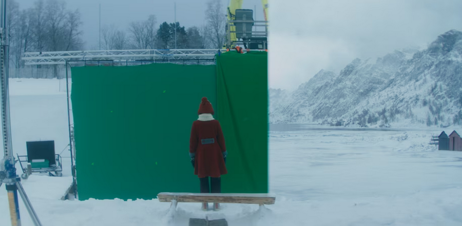 Person in red coat facing green screen with snowy mountain background.