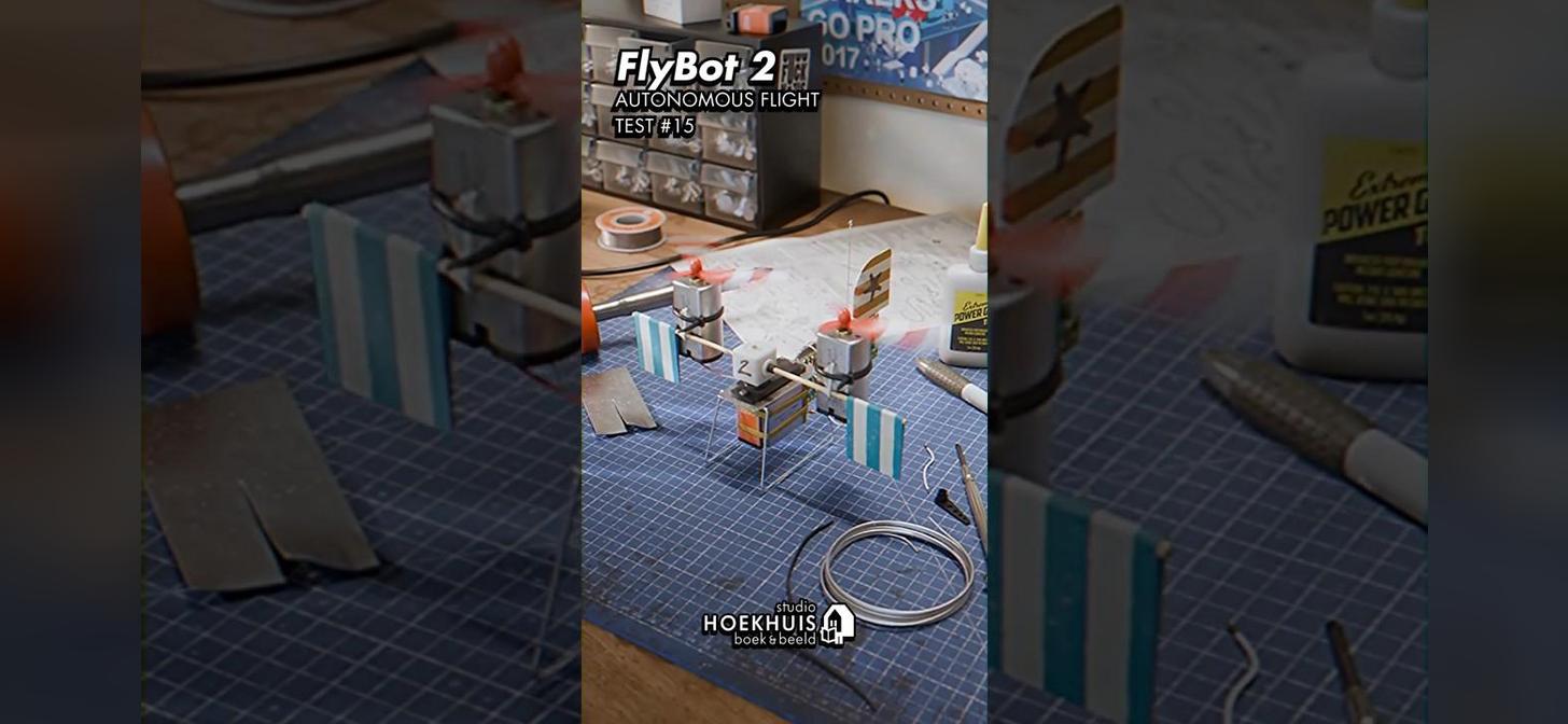 A small drone on a workbench with tools and materials, labeled "FlyBot 2 Autonomous Flight Test