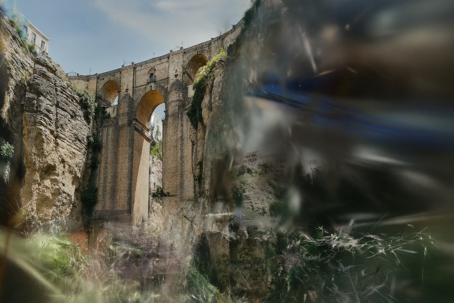 Ancient stone aqueduct with multiple arches, partially covered in greenery, set against a clear sky.
